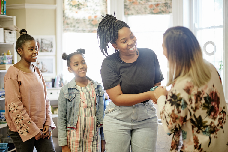 A smiling mom reaching forward to hold the hands of another happy person who is meeting her children.