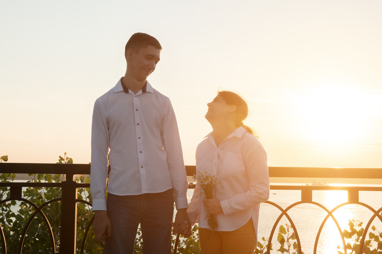 A couple standing beside a railing with a body of water behind them. One of the pair is a person with cerebral palsy.